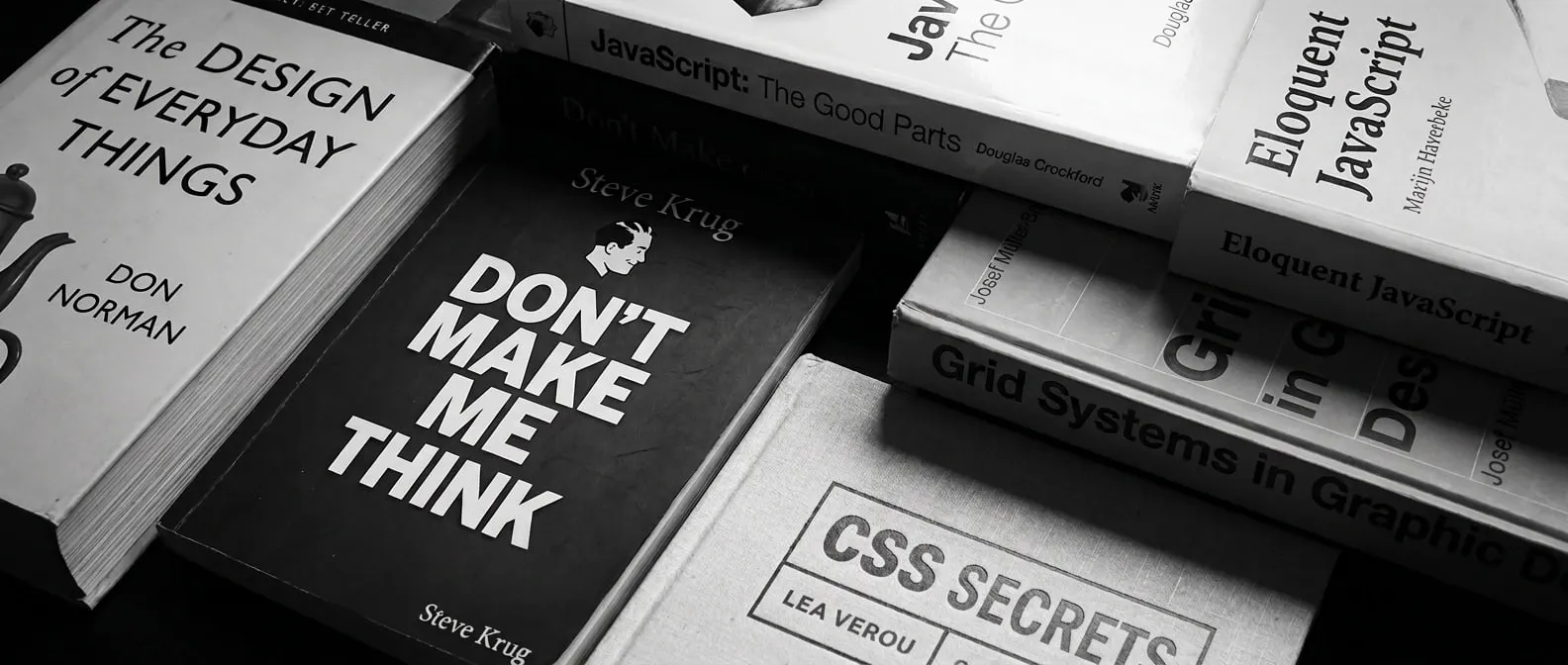 A stack of design and development books: The Design of Everyday Things, Don't Make Me Think, Grid Systems, and more